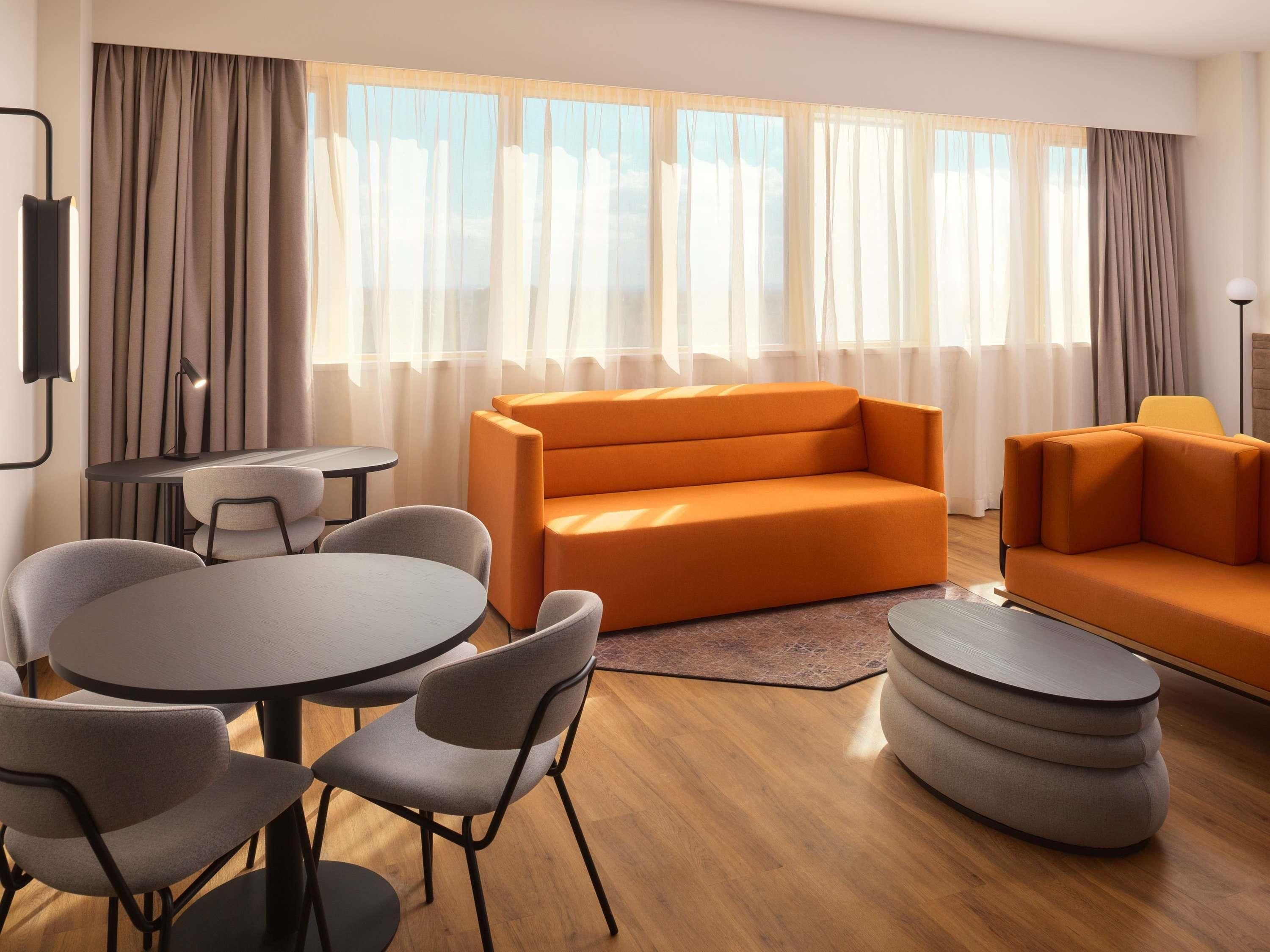 A modern living room with a sofa, chairs, a small table, and a lamp.