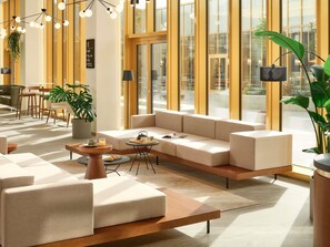 A modern lounge area with a sofa, coffee table, and chairs, large windows, and indoor plants. - Novotel Zagreb (Zagreb)