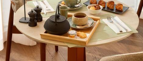 A round dining table with a tray of croissants, a cup of coffee, a teapot, and a small jar of jam.