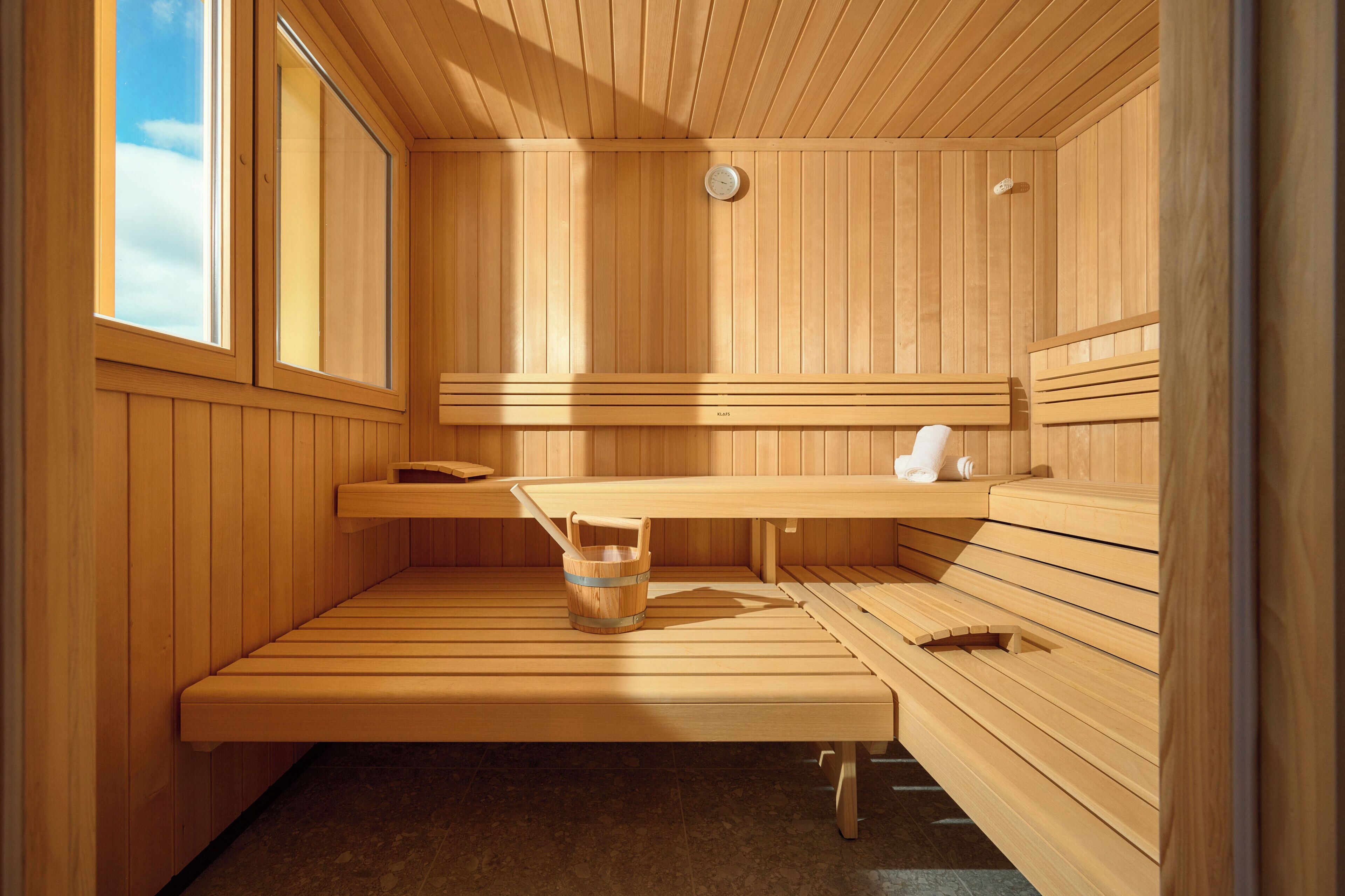 Een houten sauna met banken en een zitbank, een houten emmer en een handdoekrek.