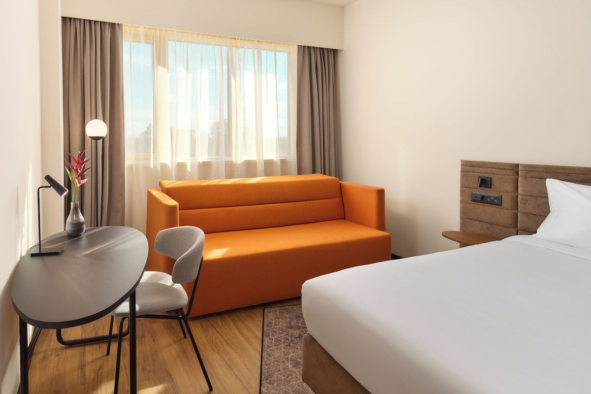A hotel room with a bed, a sofa, a desk with a lamp, and a chair.