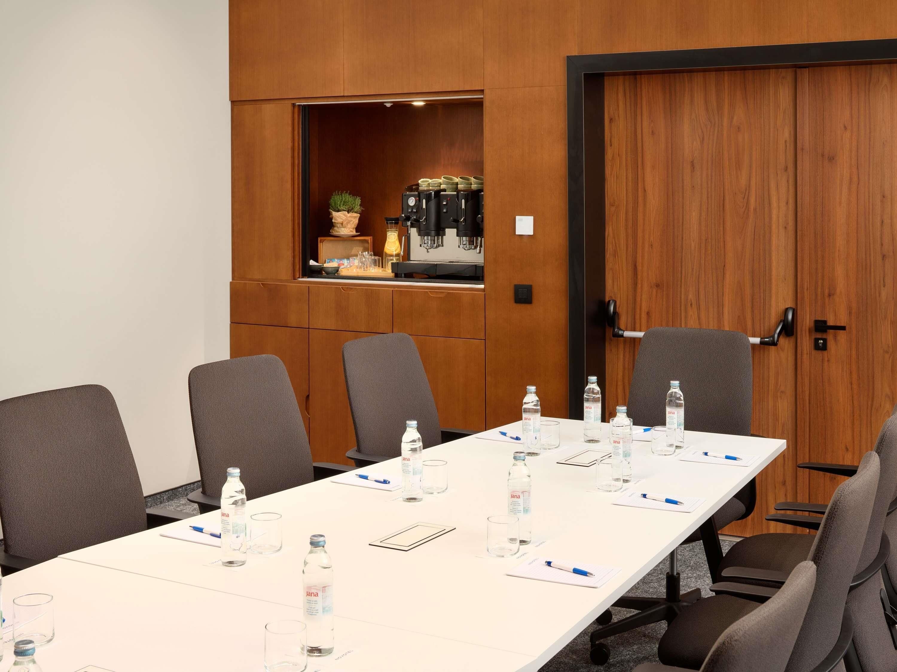A conference room with a long table, chairs, water bottles, and a coffee machine.