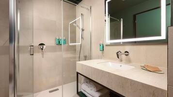 Un baño moderno con ducha de vidrio, un espejo grande y un lavamanos de mármol.