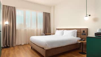 A hotel room with a bed, curtains, a bedside table with a lamp, and a nightstand with a phone.