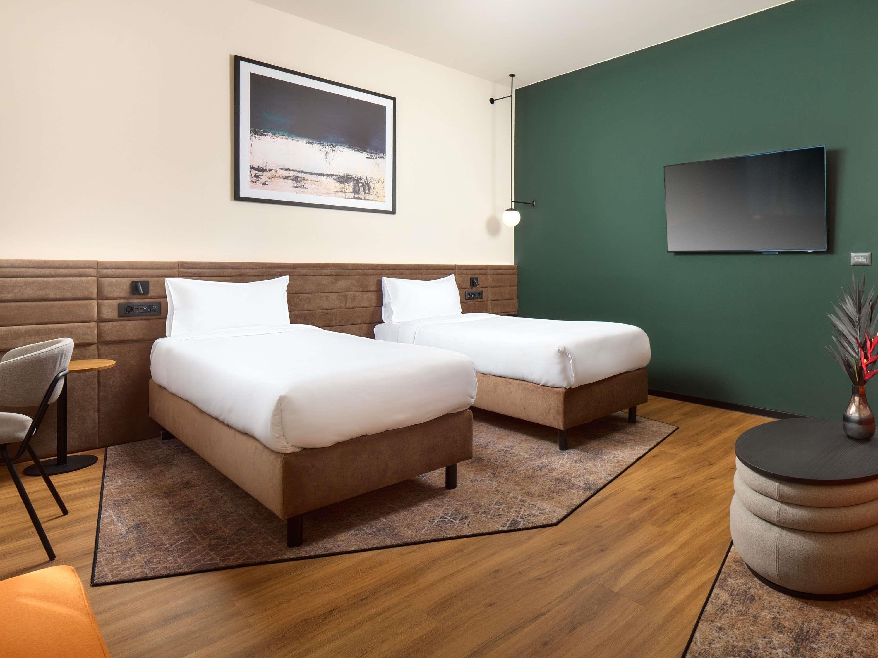 A hotel room with two beds, a TV, a framed picture, and a small table with a chair.