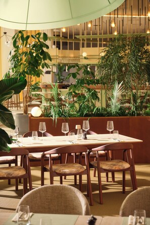 A dining area with a table set for four, surrounded by chairs, in a room with indoor plants and a modern interior design. - Novotel Zagreb - opened September 2025 (Zagreb)
