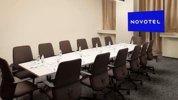 A conference room with a long table, chairs, water bottles, and a blue sign with 'NOVOTEL' on the wall.