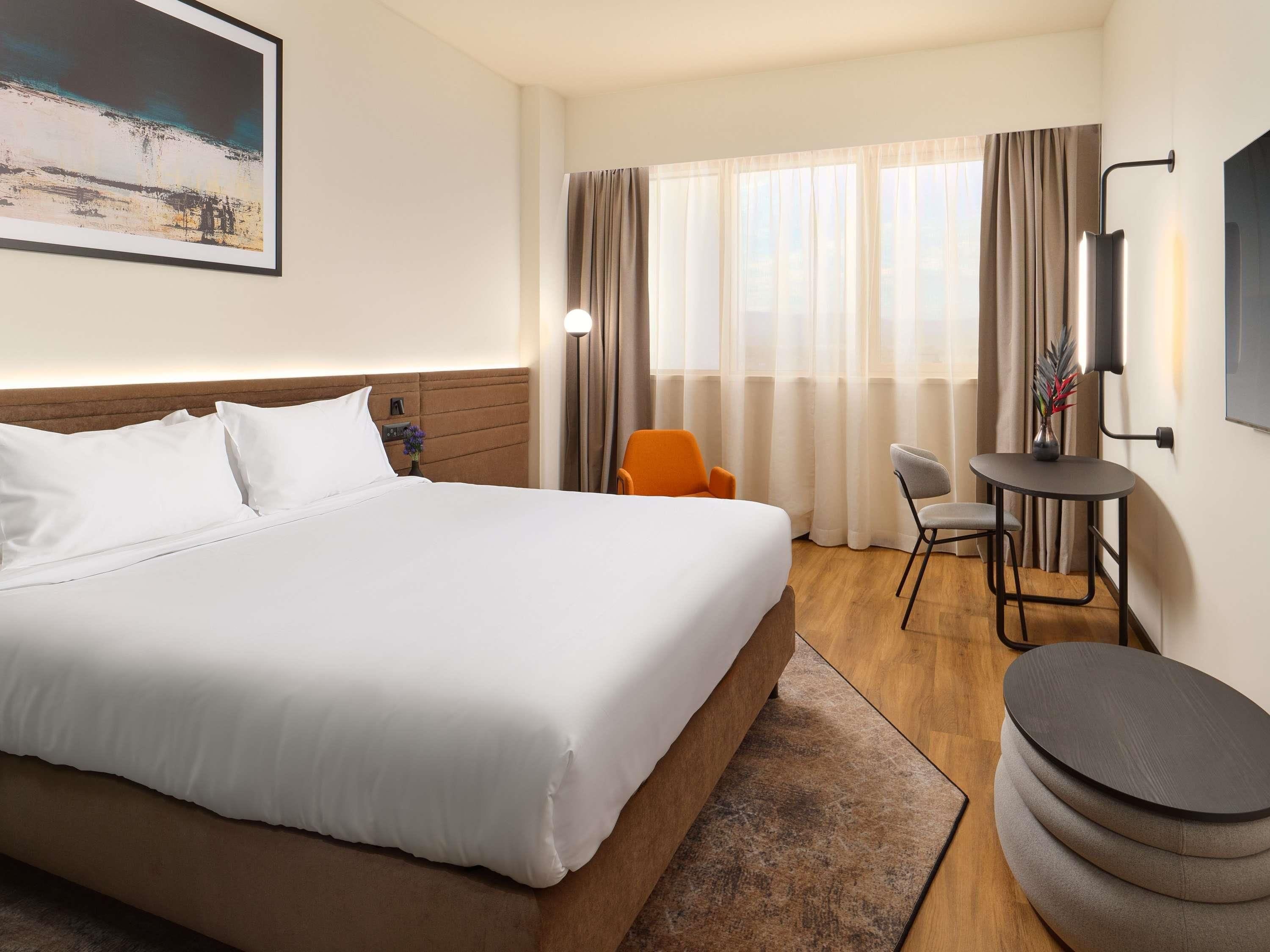 A hotel room with a large bed, a desk, a chair, and a TV.