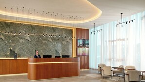 A modern reception area with a marble wall, a wooden reception desk, and a seating area with chairs and a table. - Novotel Zagreb - opened September 2025 (Zagreb)