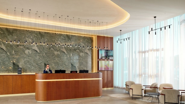 A modern reception area with a marble wall, a wooden reception desk, and a seating area with chairs and a table. - Novotel Zagreb - opened September 2025 (Zagreb)