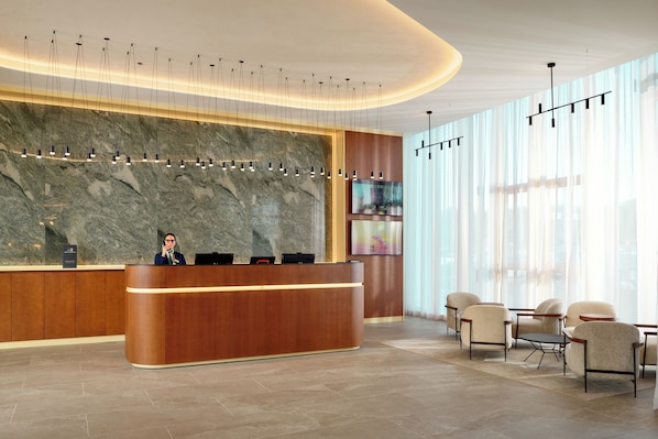 A modern reception area with a marble wall, a wooden reception desk, and a seating area with chairs and a table. - Novotel Zagreb - opened September 2025 (Zagreb)