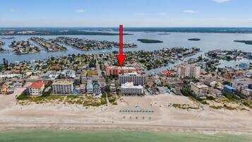 An aerial view of a coastal town with a prominent hotel marked by a red arrow, surrounded by residential areas and water bodies.