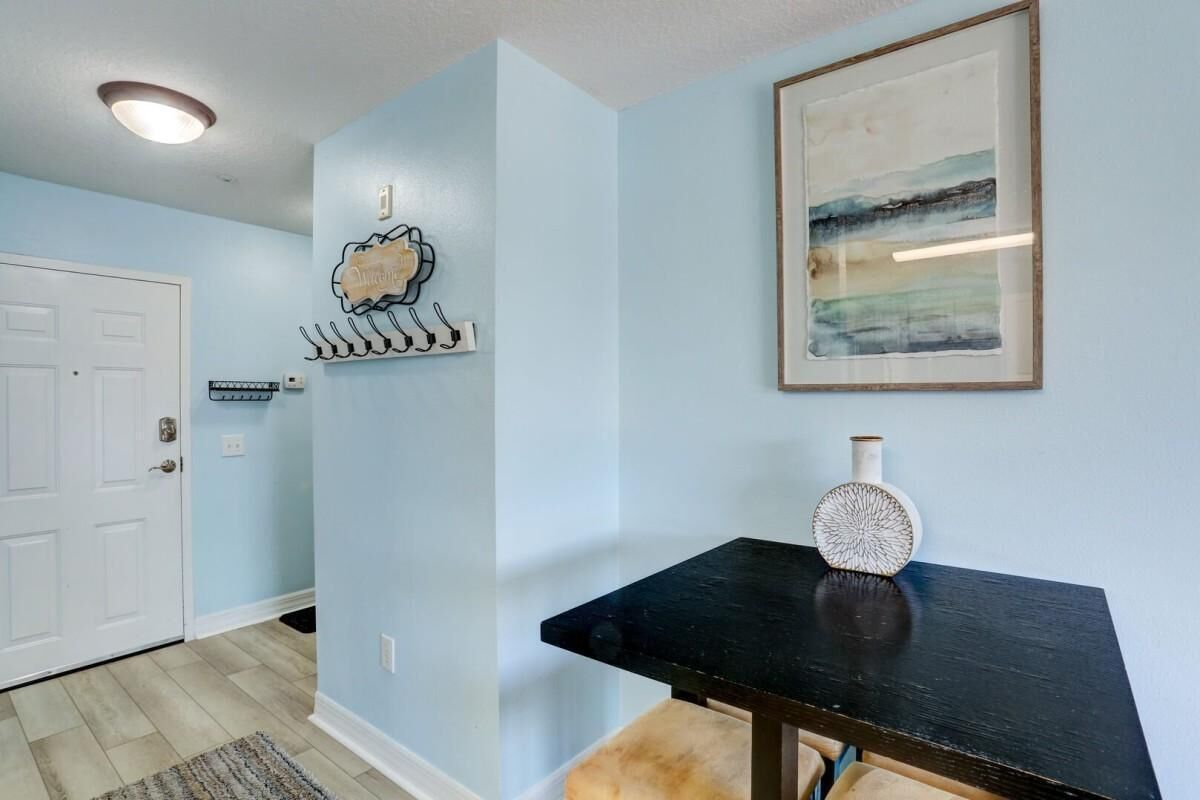 A hallway with light blue walls, a white door, a black table with a decorative vase, and a framed abstract painting.