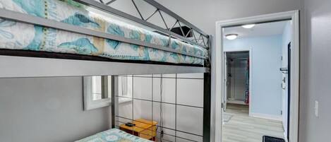 Een stapelbed met een beddeken met patroon, een klein tafeltje en een raam.