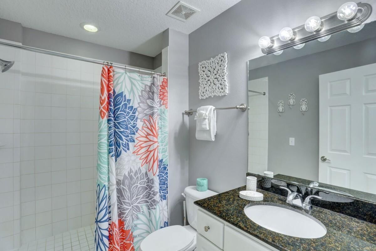 A bathroom with a shower curtain, toilet, sink, and vanity.