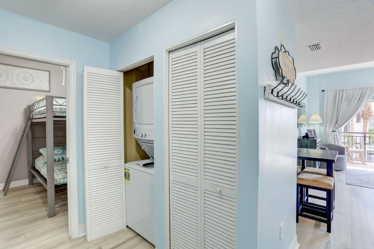 A room with a bunk bed, a washing machine, and a dining area with a table and chairs.