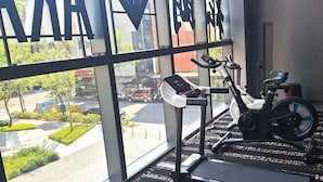 Een sportschool met trainingsapparatuur, grote ramen en uitzicht op de straat.