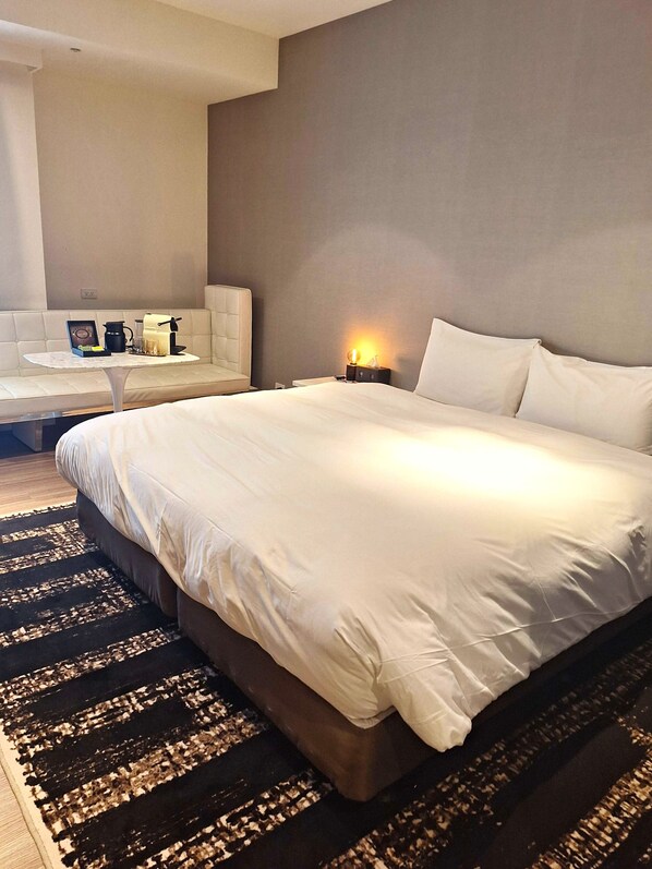 A modern hotel room with a large bed, a small table with a coffee maker, and a sofa.