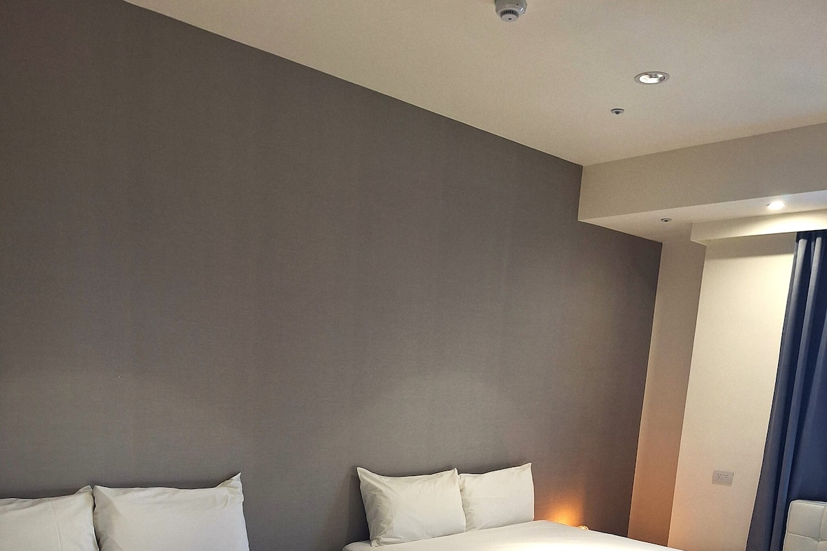 Una habitación de hotel con dos camas, una mesita de noche y una lámpara fijada a la pared.