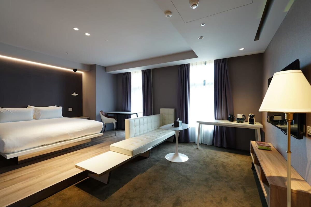 Una habitación de hotel moderna con una cama grande, un sofá, una mesita y un escritorio.