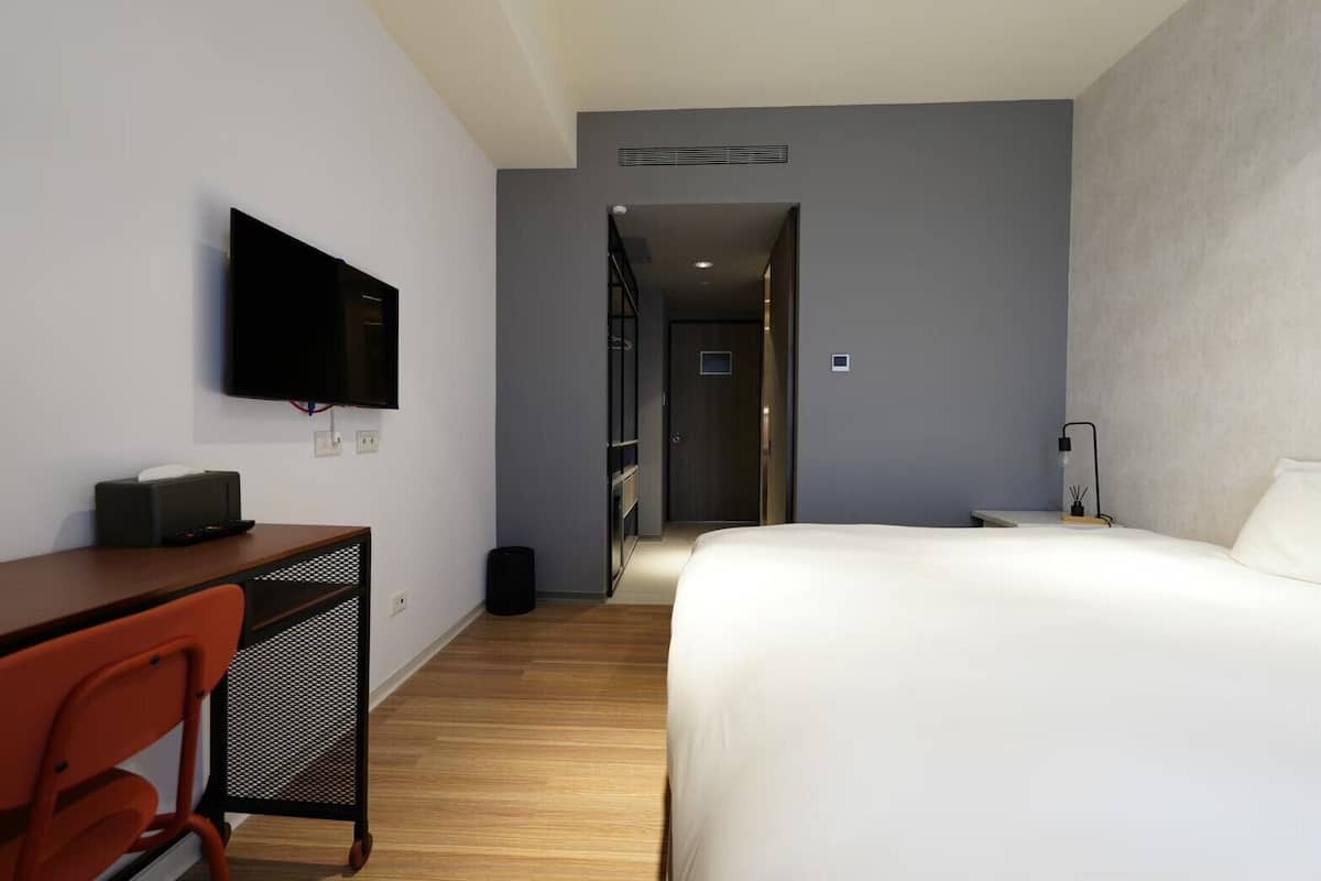 Habitación de hotel con cama, escritorio con silla, televisión y puerta que da a otra habitación.