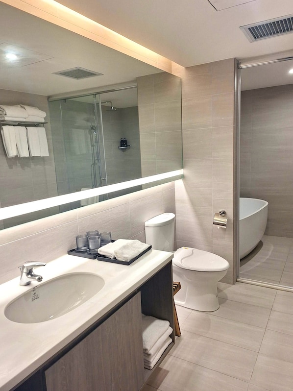 Un baño moderno con un espejo grande, un lavabo con tocador, un inodoro y una zona de ducha.