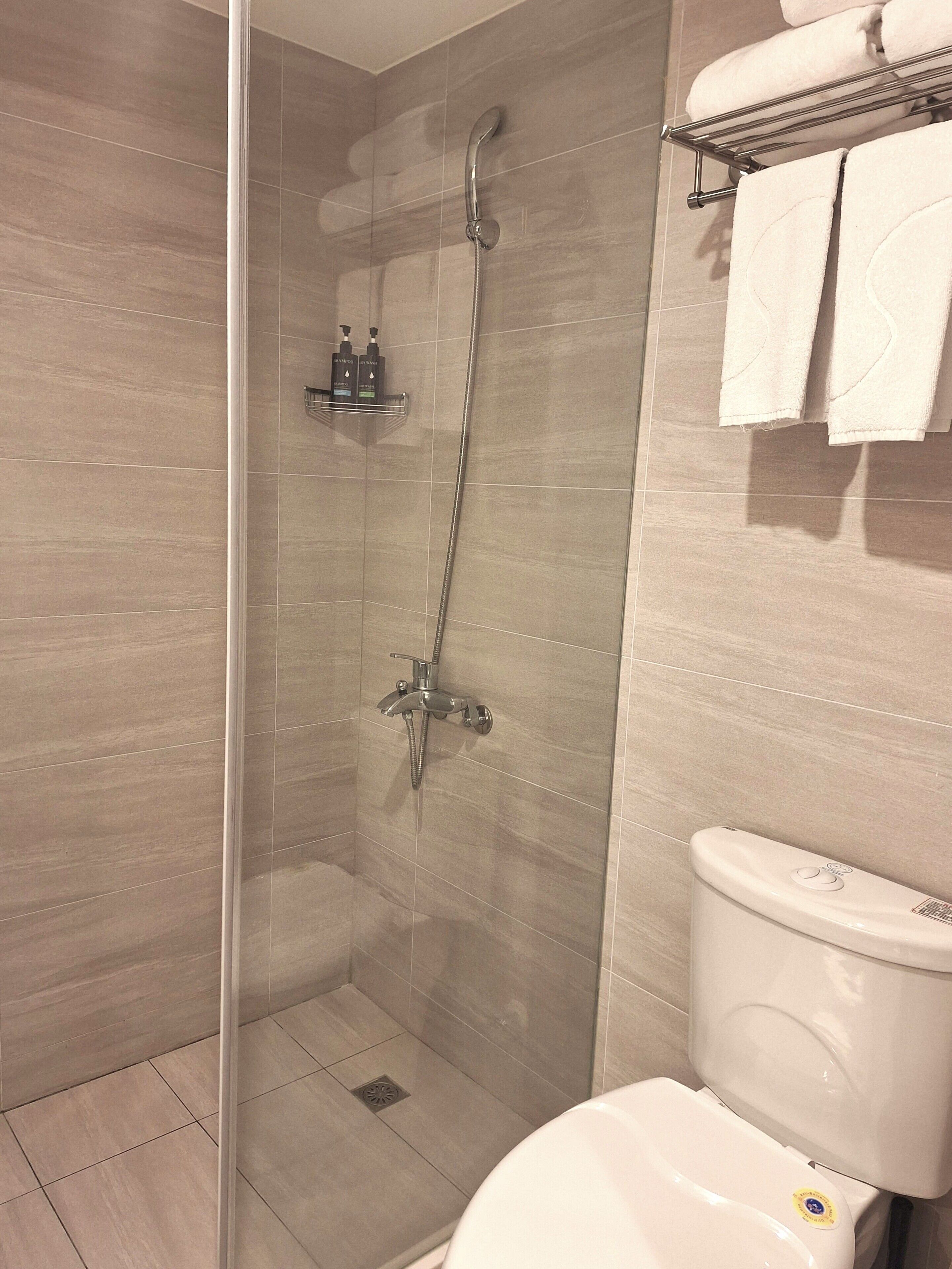 A bathroom with a glass-enclosed shower, a toilet, and a towel rack with towels.