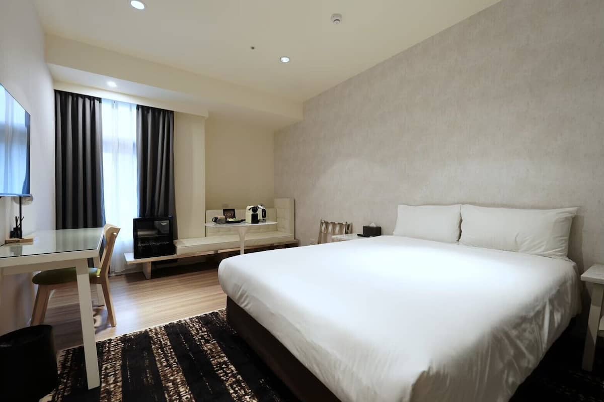 Habitación de hotel con una cama grande, un escritorio con silla, un televisor y un sofá.