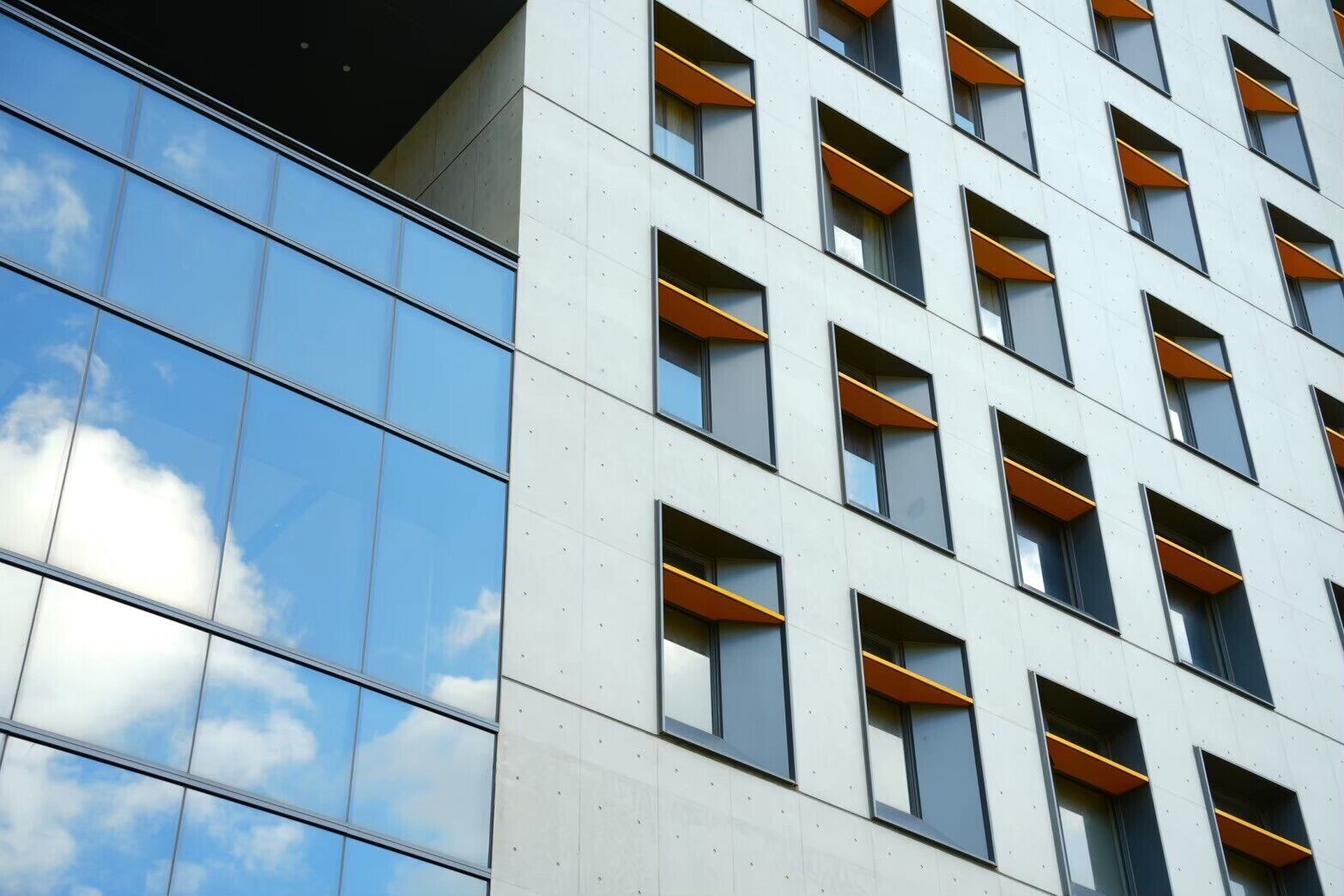 A modern building with a reflective glass facade and multiple windows with orange accents.