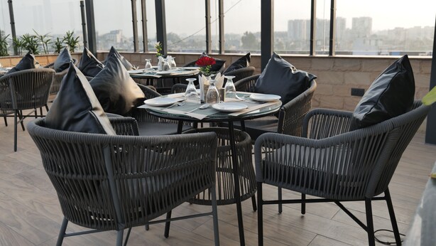 Un espace de restauration aménagé sur le toit, avec des chaises et des tables en osier, une vue sur la ville et un ciel dégagé.