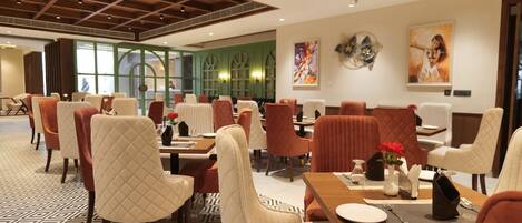 A hotel dining area with multiple tables and chairs, a patterned floor, and artwork on the walls.