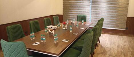 A conference room with a long table, green upholstered chairs, water bottles, and a window with blinds.