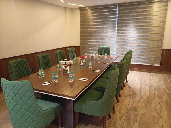 A conference room with a long table, green upholstered chairs, water bottles, and a window with blinds. - THE KEMBERLY HOTEL (Zirakpur)