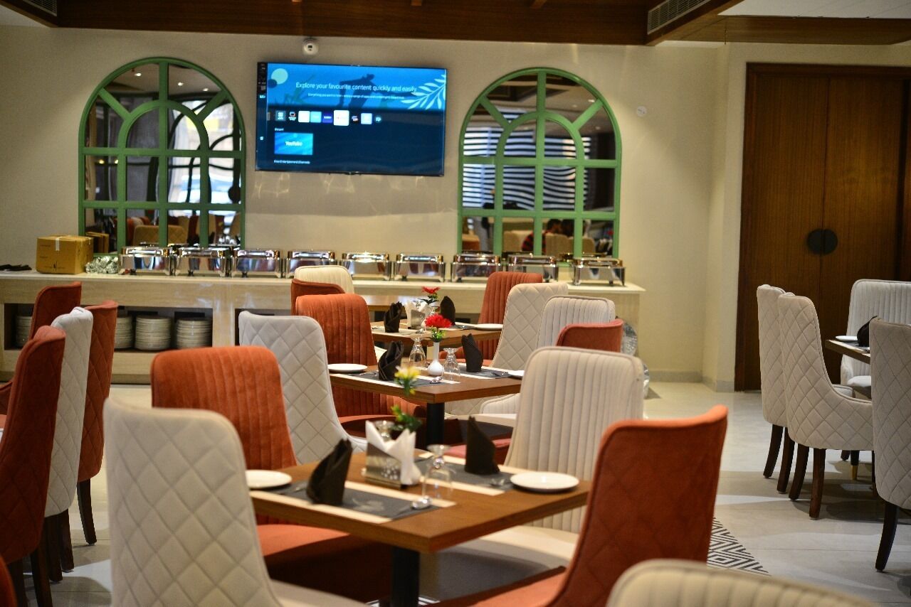 A restaurant with tables and chairs, a television screen, and arched windows.