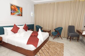 Habitación de hotel con una cama grande, dos sillas, una mesita y un cuadro en la pared.