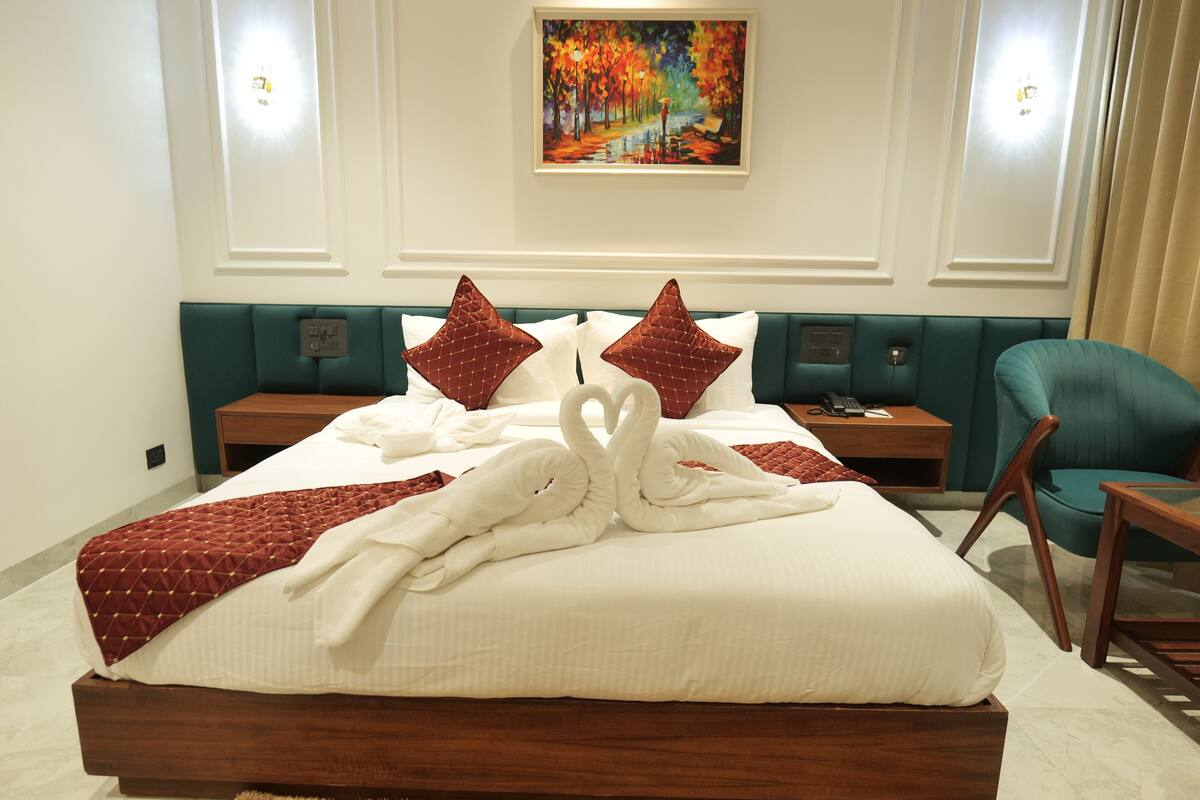 Un lit bien fait, avec une couette blanche et des oreillers rouges, une tête de lit recouverte d’un tissu turquoise et un tableau accroché au-dessus du lit.
