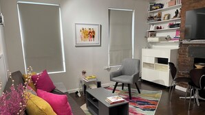 Ein modernes Wohnzimmer mit grauem Sofa, bunten Kissen, einem Couchtisch und einem Bücherregal.