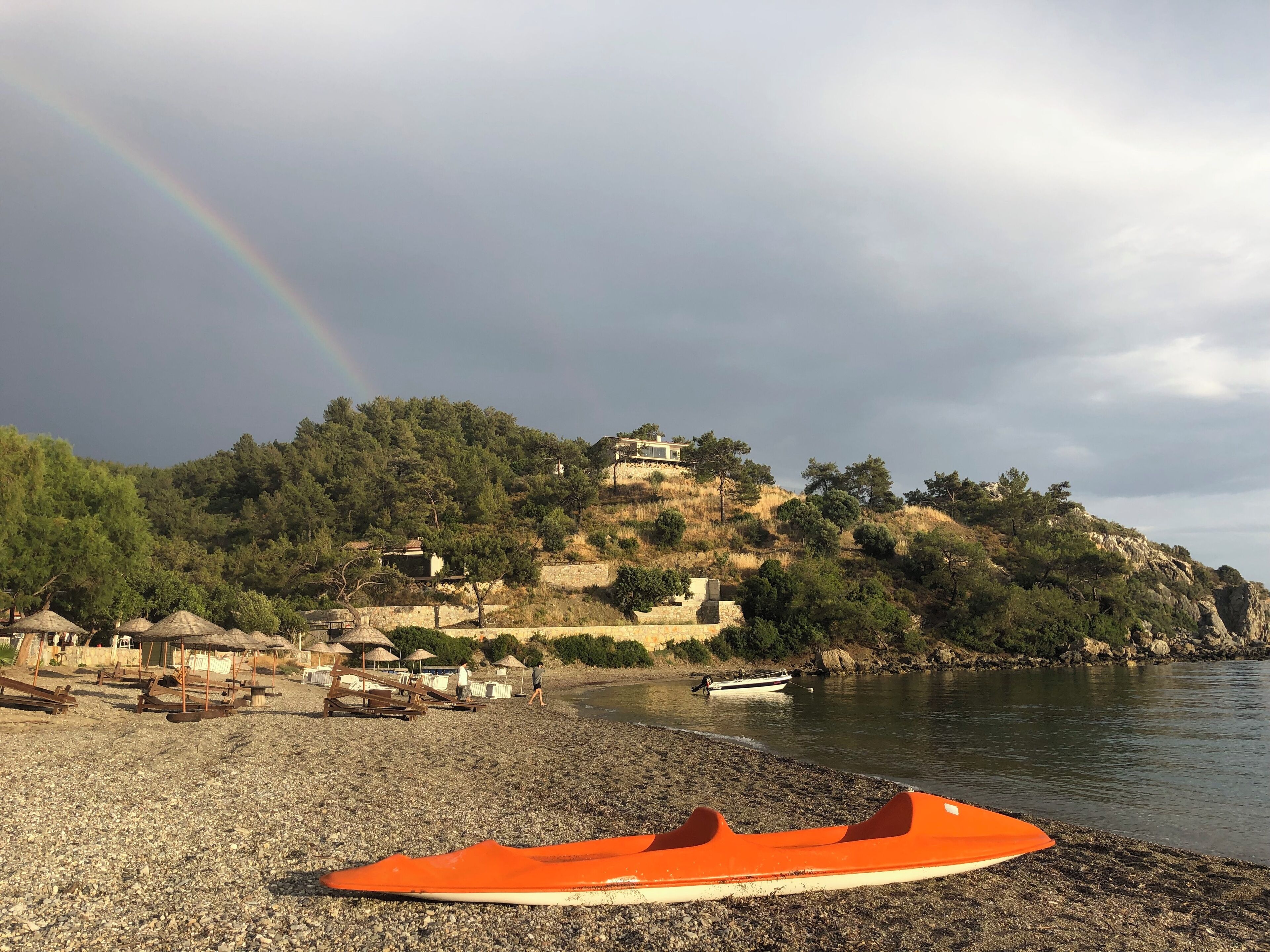 A beach with a rocky shore, a small boat, and a house on a hill.