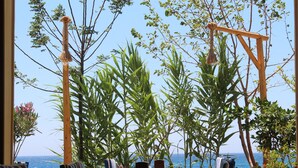 A table set for dining with chairs, a view of the sea, and lush greenery. - Incekum Pansiyon (Maziköy)