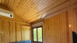 A wooden-paneled room with a bed, a nightstand, a window, and an air conditioning unit. - Incekum Pansiyon (Maziköy)