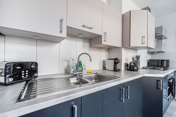 A modern kitchen with a stainless steel sink, a toaster, a coffee maker, and a microwave.