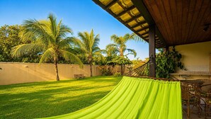 Eine Hängematte unter einer Holzpergola, ein Rasen und ein Essbereich mit Korbmöbeln.