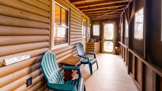 A log cabin with a porch, wooden walls, and a table with chairs.