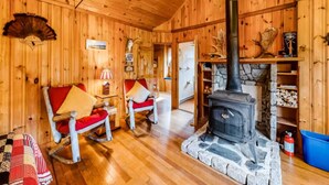 A wooden cabin interior with a stone fireplace, two rocking chairs, and a log shelf.