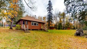A wooden cabin with a porch, surrounded by trees and a grassy yard.