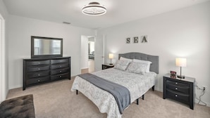 A bedroom with a bed, nightstands, a dresser, a mirror, and a wall with the word 'SEA' spelled out.