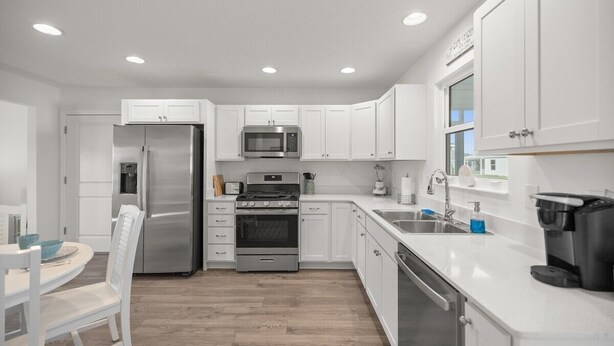 A modern kitchen with white cabinets, stainless steel appliances, and a wooden floor.