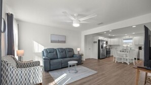 A modern living room with a sofa, a dining table, and a kitchen in the background.