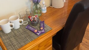 A wooden desk with a black chair, a vase with purple flowers, a bottle of hand sanitizer, and two instant coffee packets. - Rooms at the Huntsman Inn (Falfield)