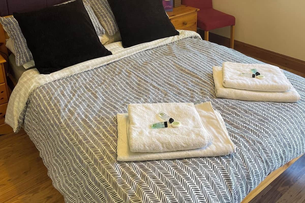 Una cama bien hecha con una colcha estampada, dos almohadas y dos toallas dobladas sobre la cama.